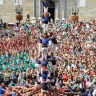 A vibrant display of a human tower made of participants in colorful costumes, surrounded by an enthusiastic crowd during a festive celebration.