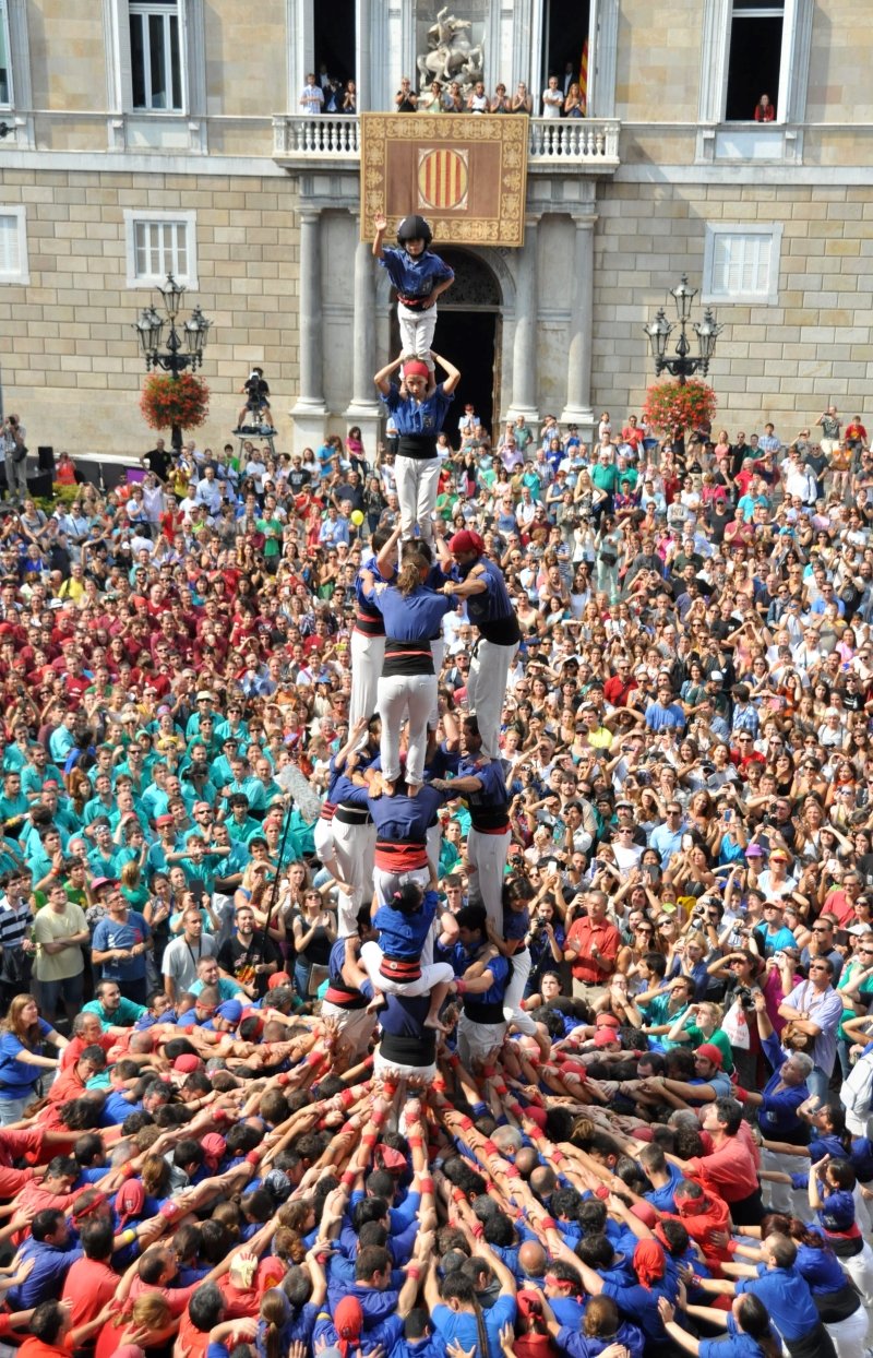 A vibrant display of a human tower made of participants in colorful costumes, surrounded by an enthusiastic crowd during a festive celebration.