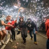 A vibrant street scene depicting a lively celebration with people dancing and dodging sparks from a firework display.