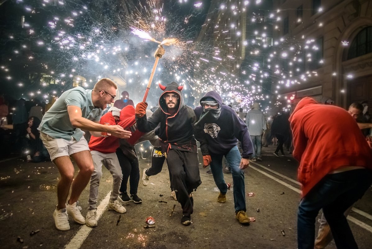 A vibrant street scene depicting a lively celebration with people dancing and dodging sparks from a firework display.