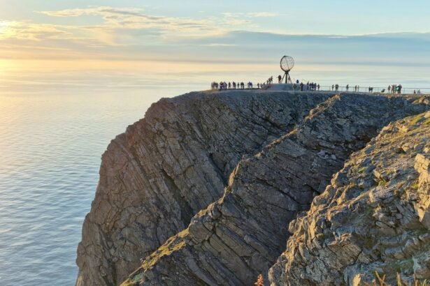 A breathtaking view of the Nordkapp cliff, with visitors gathered near the globe monument overlooking the serene ocean during sunset.