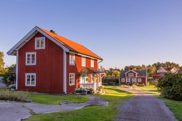 A picturesque view of a red wooden house with a vibrant roof, surrounded by greenery and other charming houses under a clear blue sky.
