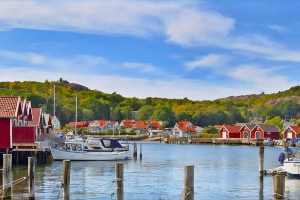 A serene view of a coastal town featuring red-roofed houses, boats docked in the water, and lush green hills under a clear blue sky.